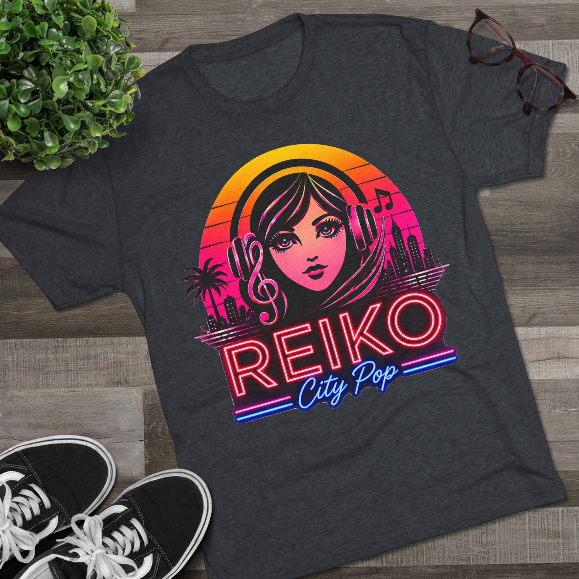 Front view of the Reiko Takahashi City Pop Sunset Logo Tee in Vintage Navy, printed on a premium Next Level tri-blend T-shirt and displayed in a styled flat lay with sneakers, eyeglasses, and a green plant. Features retro neon artwork inspired by the song "Sunset Road."