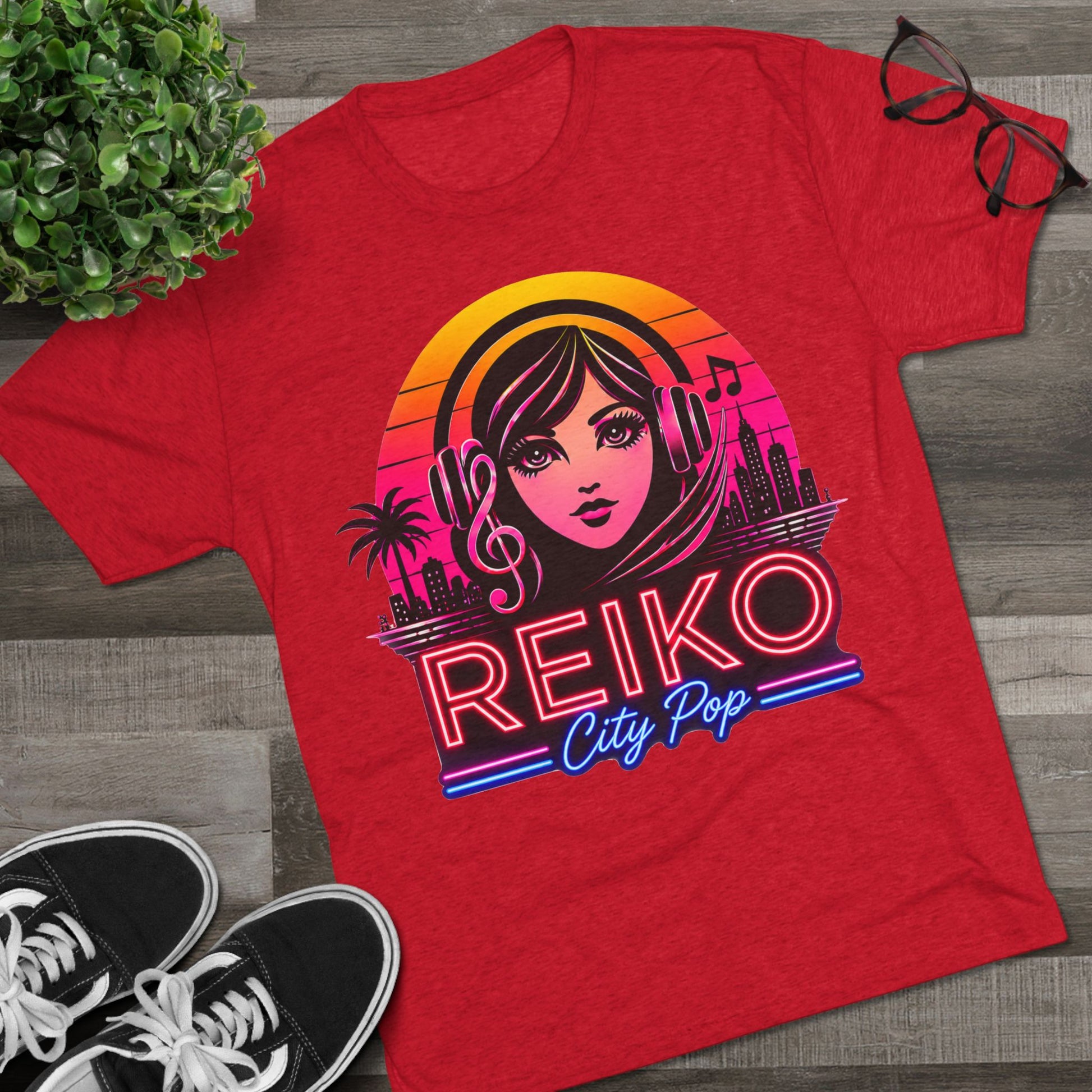 Front view of the Reiko Takahashi City Pop Sunset Logo Tee in Vintage Red, printed on a premium Next Level tri-blend T-shirt and displayed in a styled flat lay with sneakers, eyeglasses, and a green plant. Features retro neon artwork inspired by the song "Sunset Road."