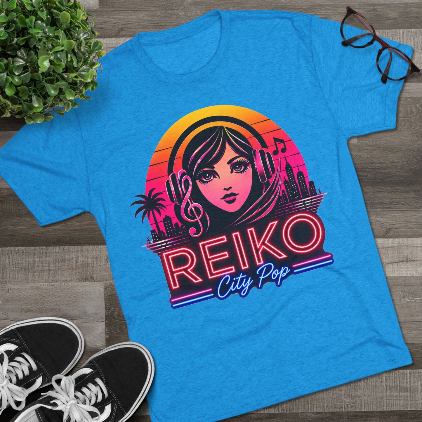Front view of the Reiko Takahashi City Pop Sunset Logo Tee in Vintage Turquoise, printed on a premium Next Level tri-blend T-shirt and displayed in a styled flat lay with sneakers, eyeglasses, and a green plant. Features retro neon artwork inspired by the song "Sunset Road."